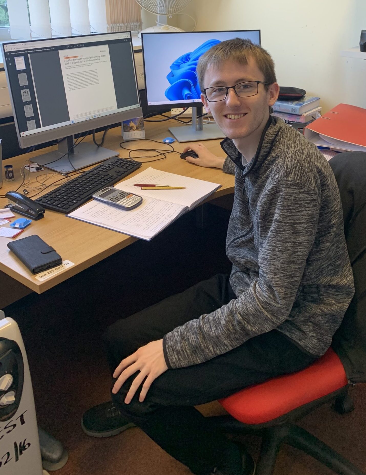 Liam sat at his desk. Behind him is his computer and notebook.