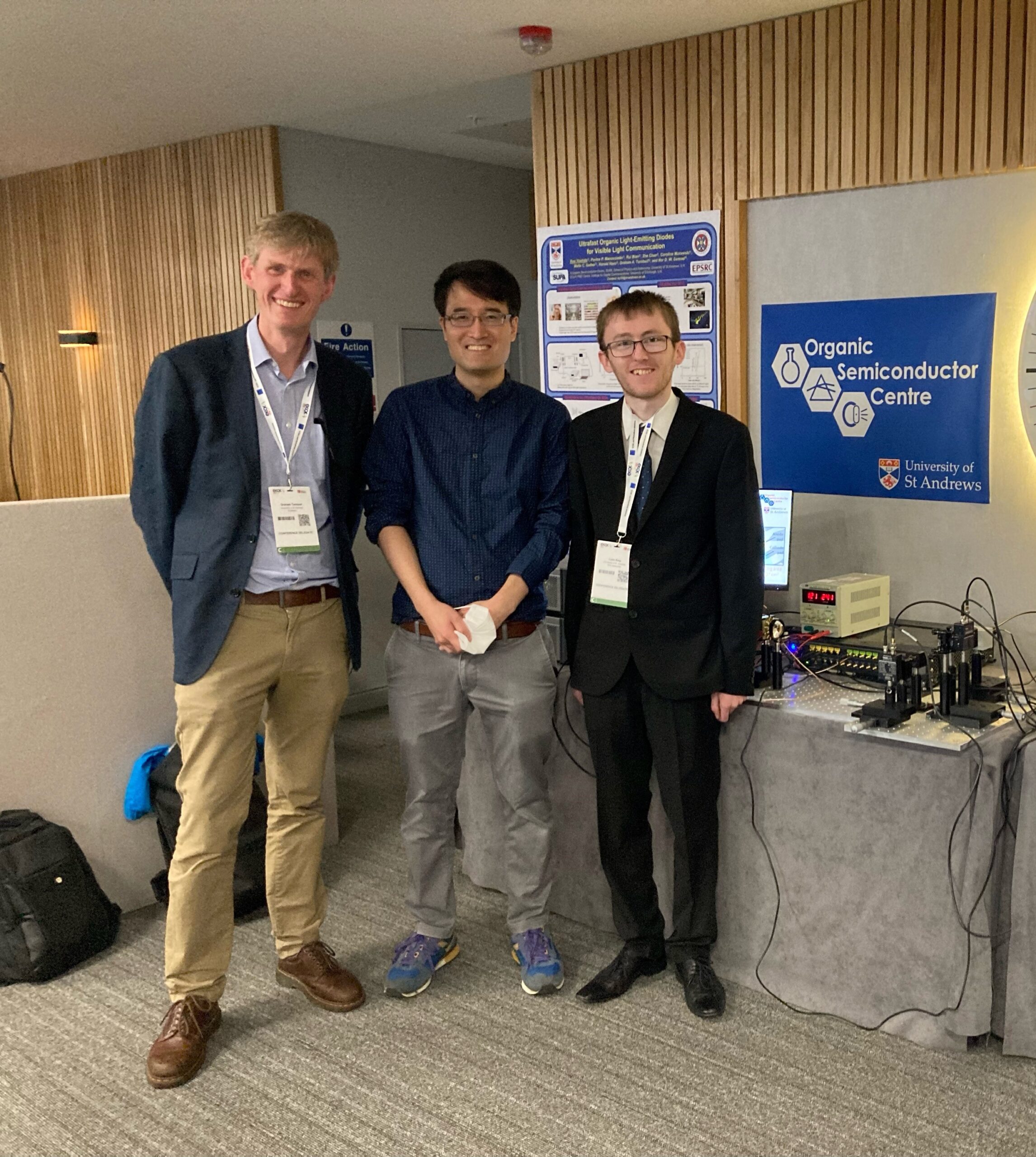 From left to right. Graham, Kou and Liam. on the right is some scientific equipment and behind them is a conference poster