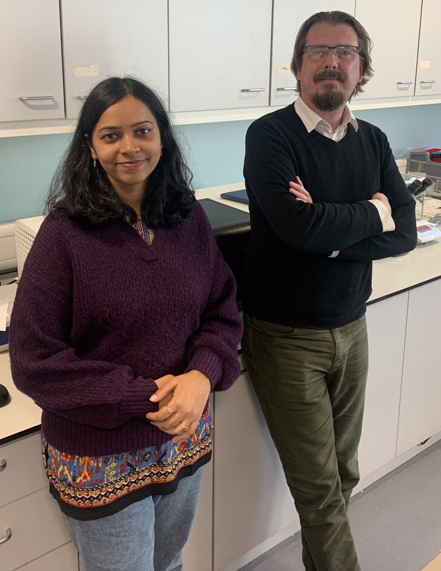 Sagarika (left) and Ross (right) they are stood in a lab in front of a workbench.