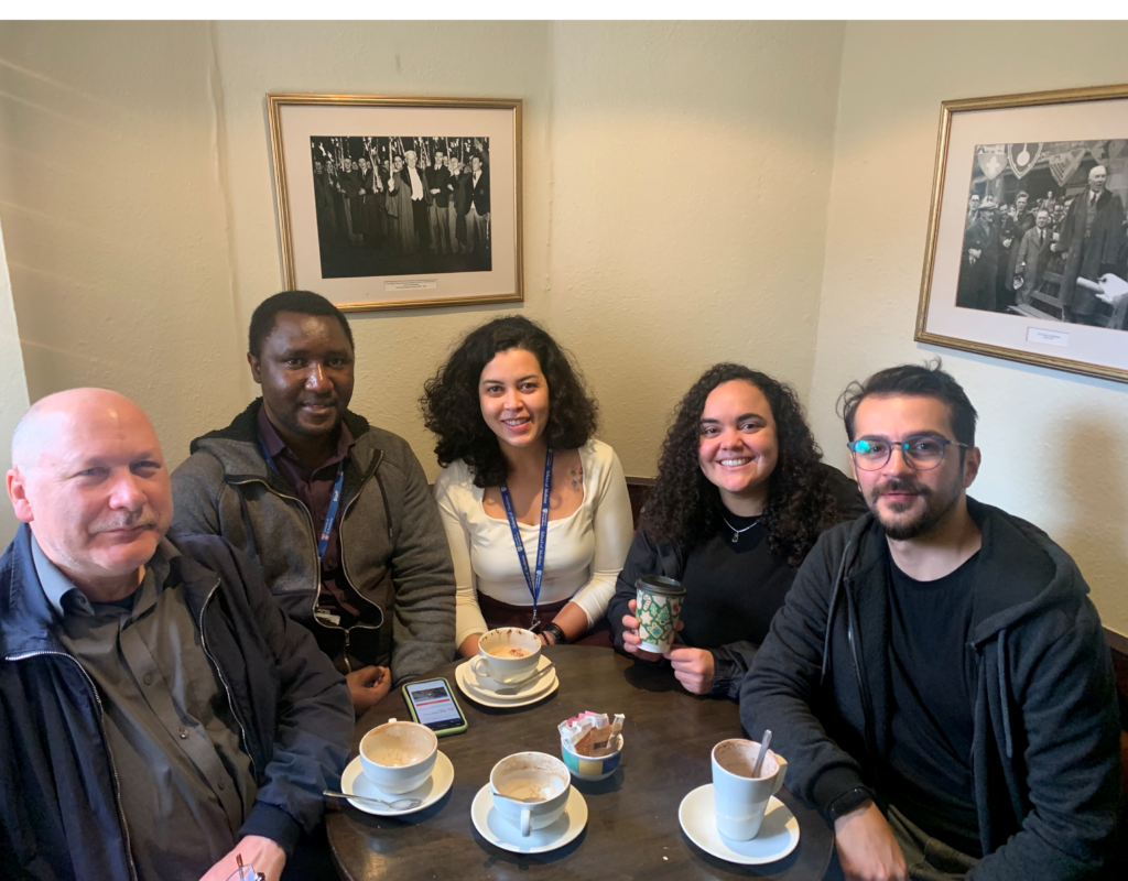 From left to right: Arvydas, Edward, Marianna, Michele and Saban. Sat drinking coffee together, with old pictures in the background.